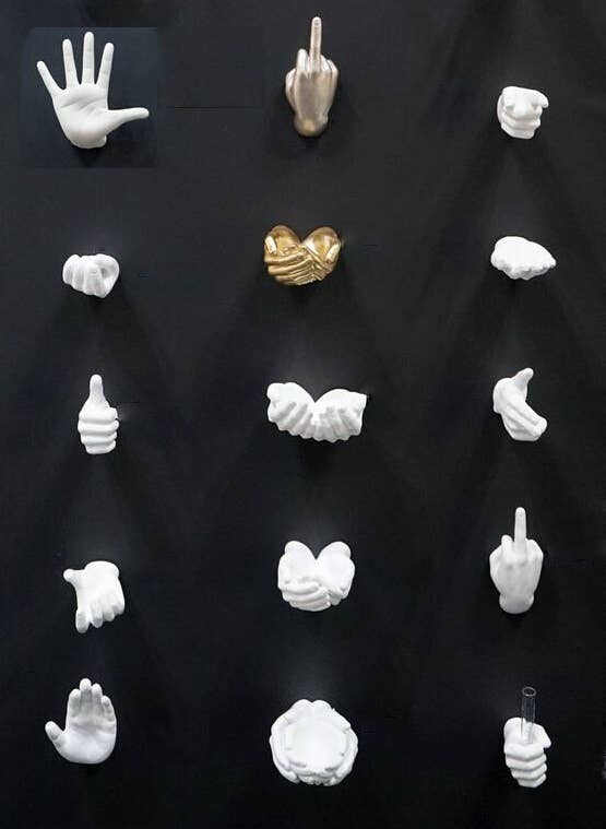 Talk to the hand wall mount among a grid of white and gold ceramic hand gesture sculptures on black