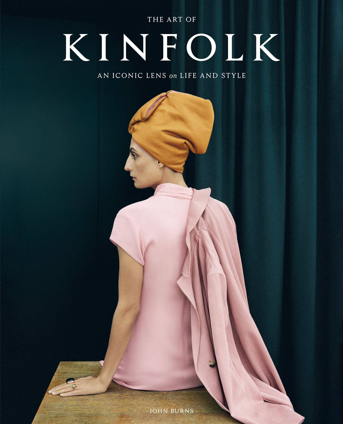 Full front cover of The Art of Kinfolk, An iconic lens on life and style, with a dark teal curtain backdrop