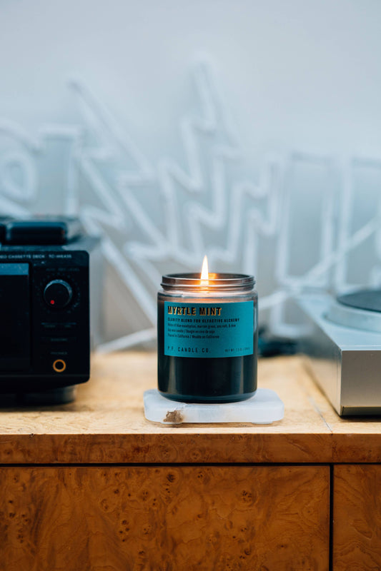 Lit Myrtle Mint candle on a white stone coaster on a burl wood cabinet beside a tape deck