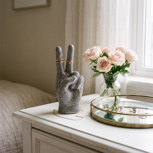 Rhinestone peace sign hand on a dresser with rings on its fingers and pink roses
