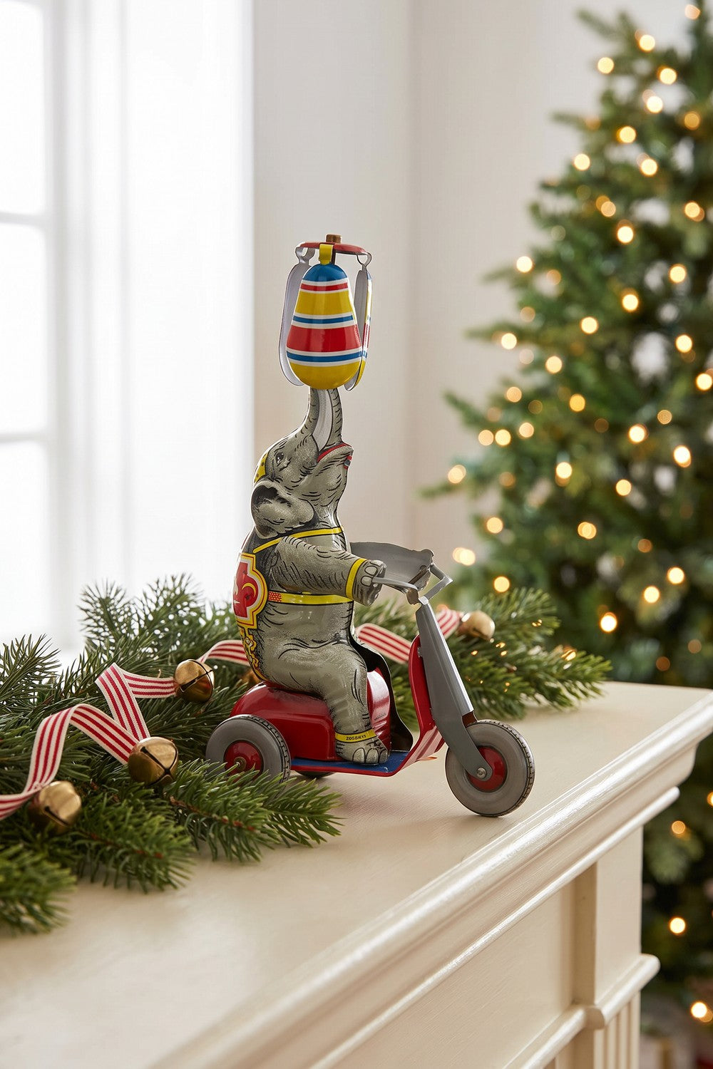 Tin circus elephant on scooter on a holiday mantel with evergreen garland
