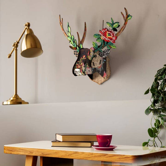 Floral deer head trophy on a gray wall above a white desk with books, a red cup and a brass lamp