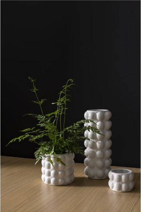 Matte white Bubble vase and two bubble pots, one holding a fern, on a wood table against a black wall