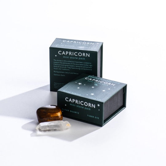 Capricorn mini stone pack text on dark green boxes with Capricorn constellation pattern. Clear quartz and polished tiger eye stones in front.