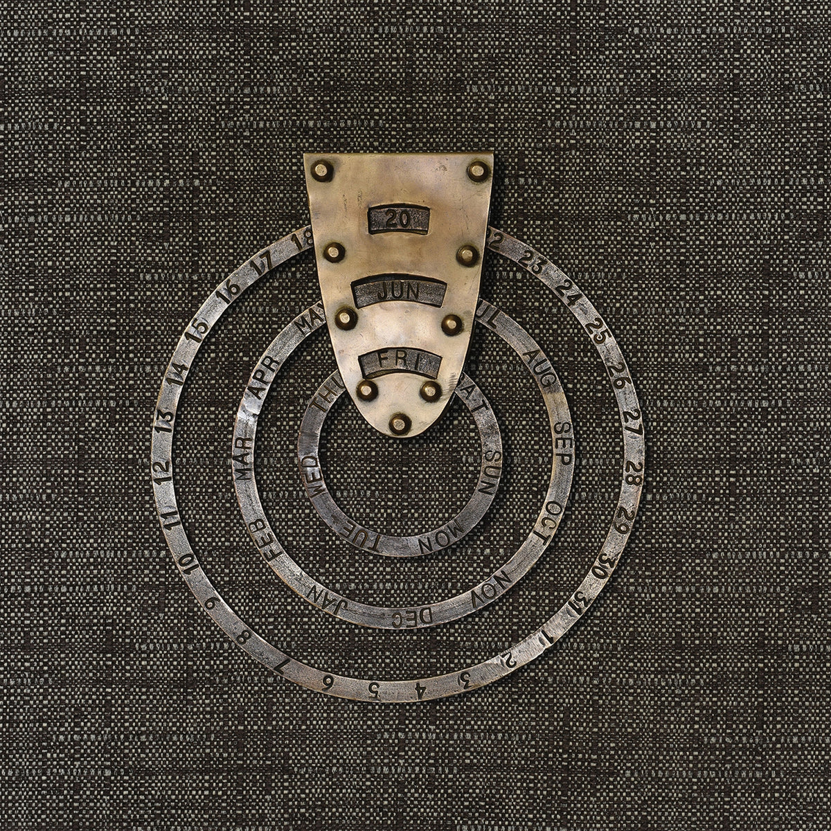 Perpetual circular calendar in antiqued brass hung on a dark woven backdrop, set to 20 Jun Fri