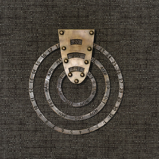 Perpetual circular calendar in antiqued brass hung on a dark woven backdrop, set to 20 Jun Fri