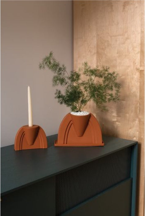 DEV planter holding a feathery fern and DEV candle holder with a white taper on a dark green cabinet