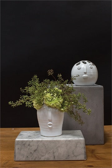 Tall Picasso bud vase with green hydrangea on marble, round vase on a gray block behind it