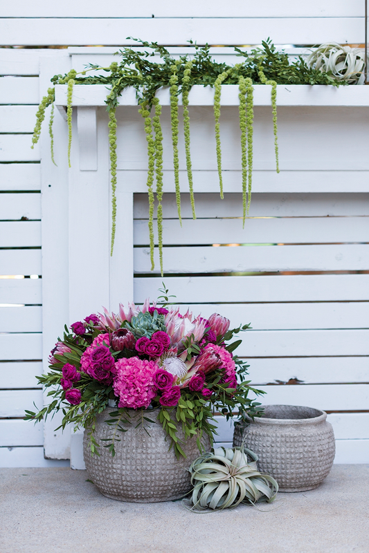 Kemble pots on a patio, the larger filled with pink hydrangea and protea, beside an air plant and white fence