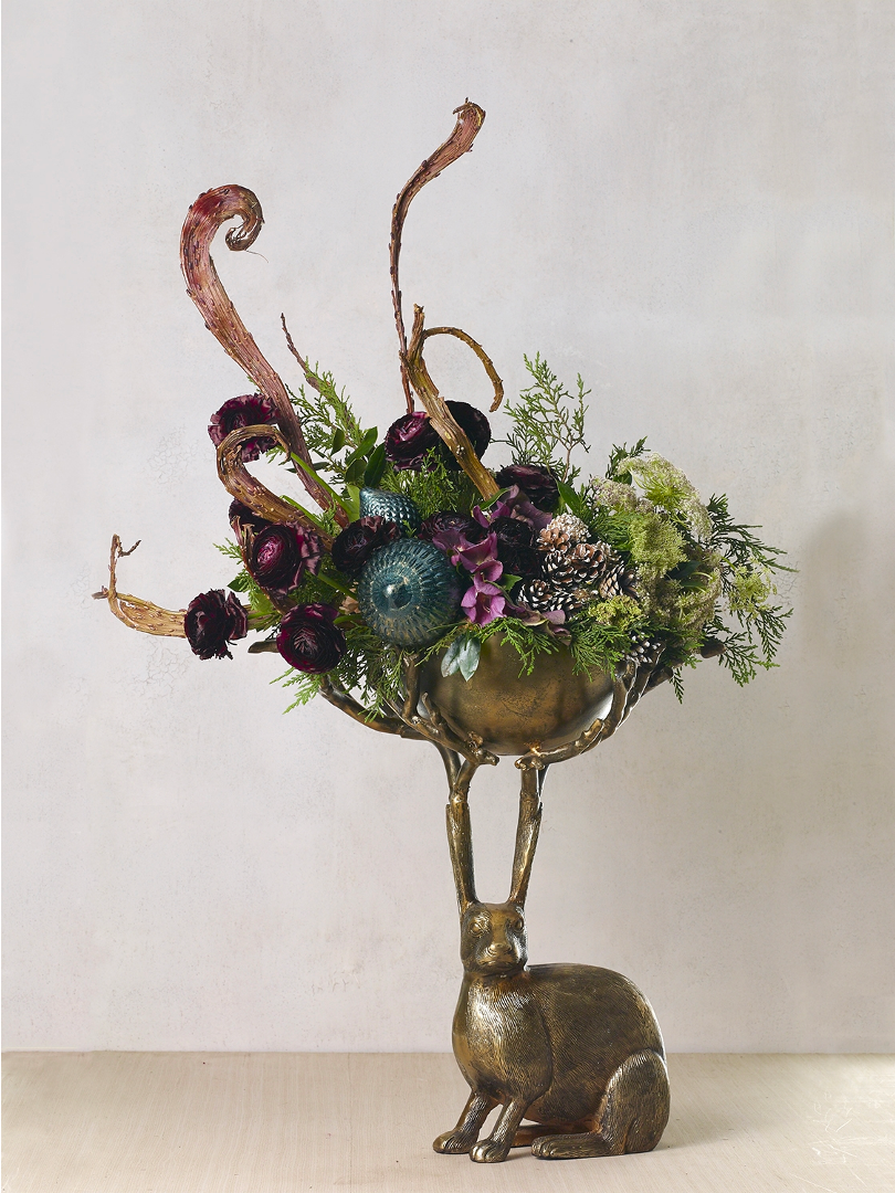 Eric branch bowl holding a tall arrangement of burgundy ranunculus, greenery, pinecones and a teal ornament