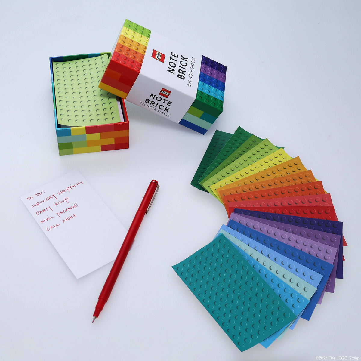 LEGO Note Brick box open with brick-patterned note sheets fanned out in rainbow colors beside a red pen