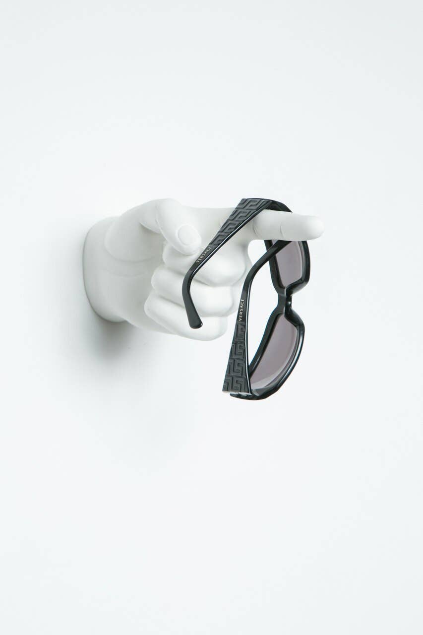 White pointing hand wall hook holding a pair of black sunglasses draped over the finger