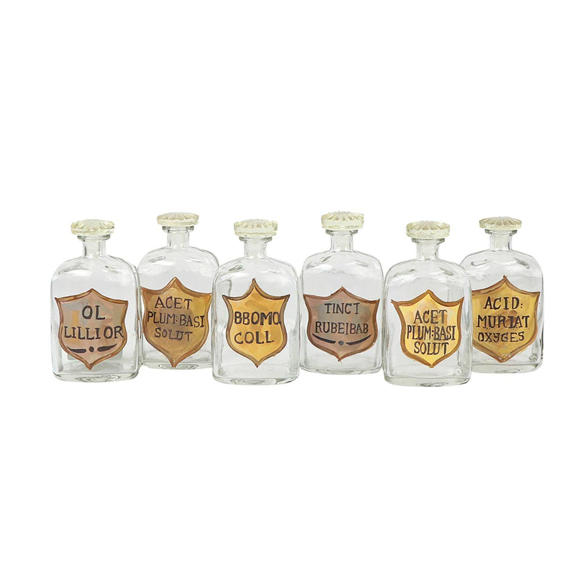 Six clear glass apothecary bottles with stoppers and hand-painted gold and copper shield labels in a row