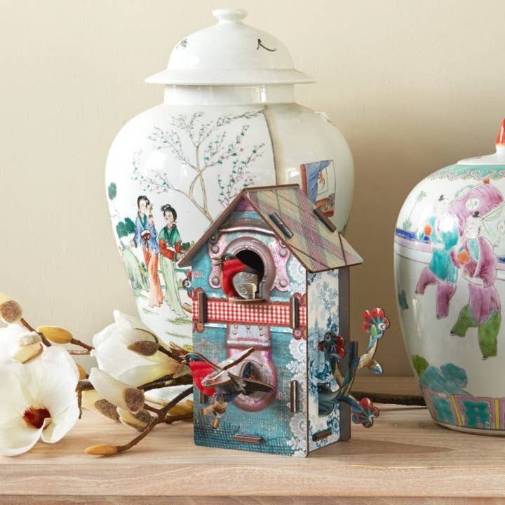 Playmates bird house standing on a wooden shelf in front of two painted porcelain ginger jars