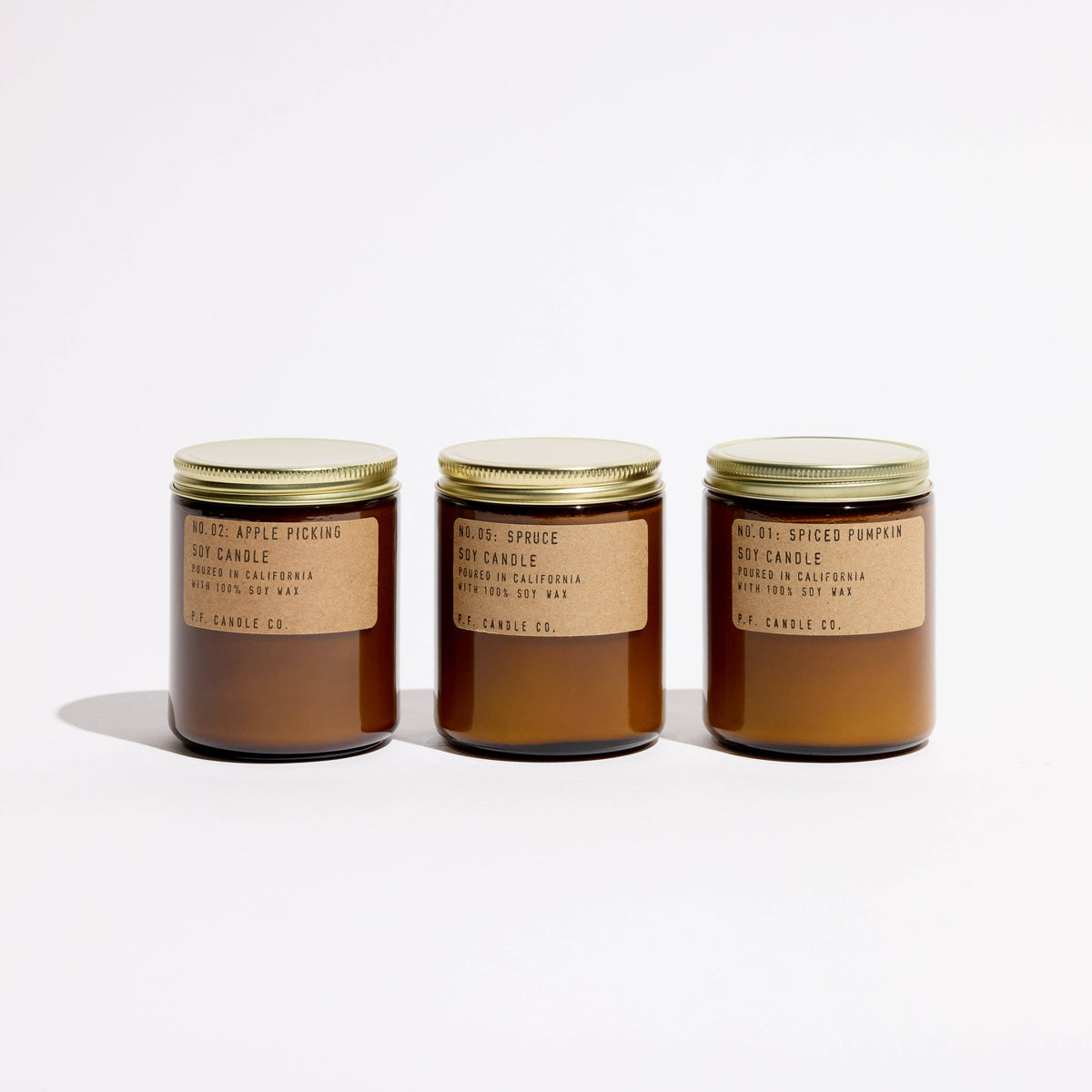 Apple Picking, Spruce and Spiced Pumpkin soy candles in a row, amber jars with gold lids and kraft labels