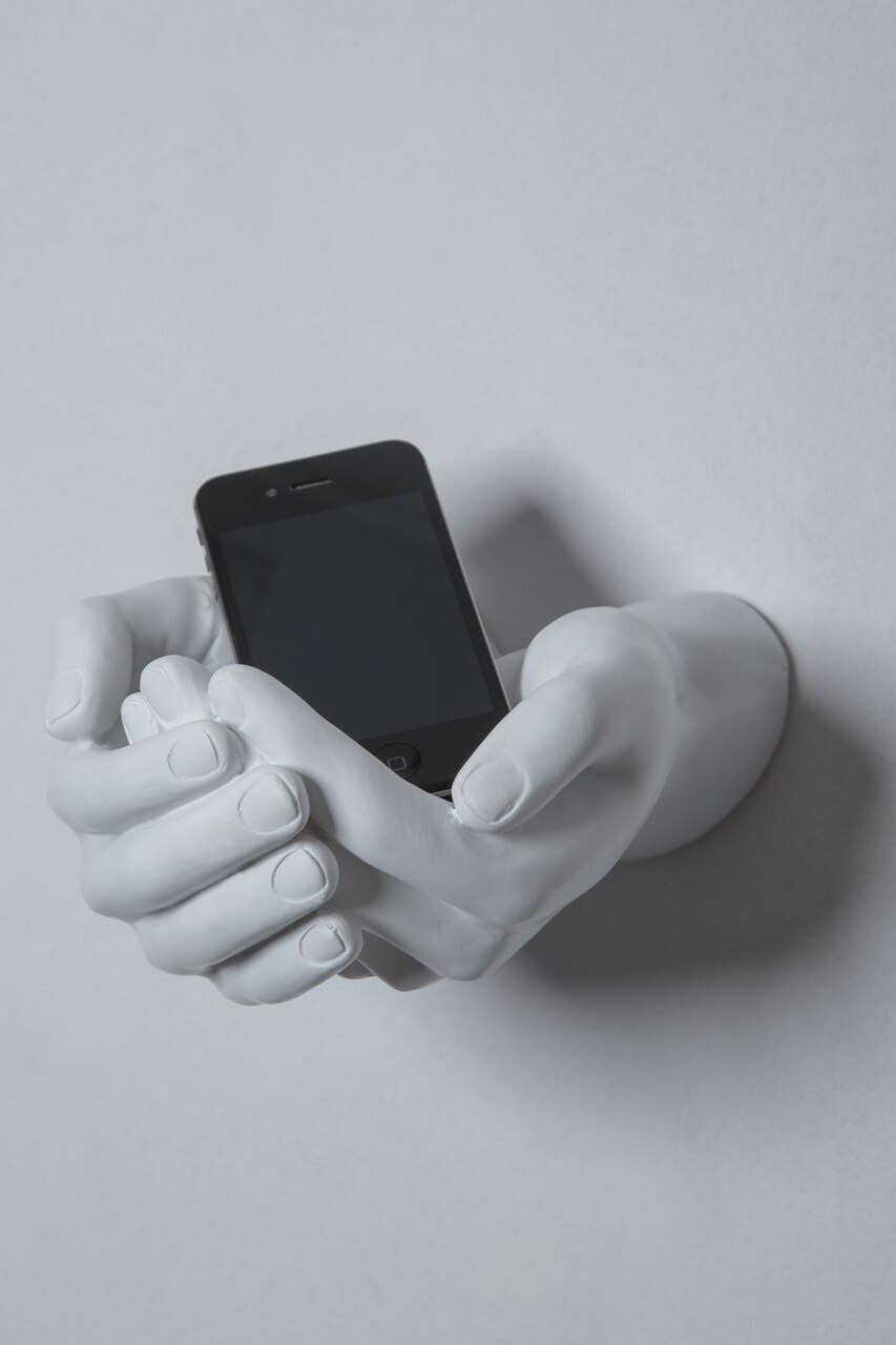 White criss-cross hands wall sculpture holding a black smartphone, angled side view