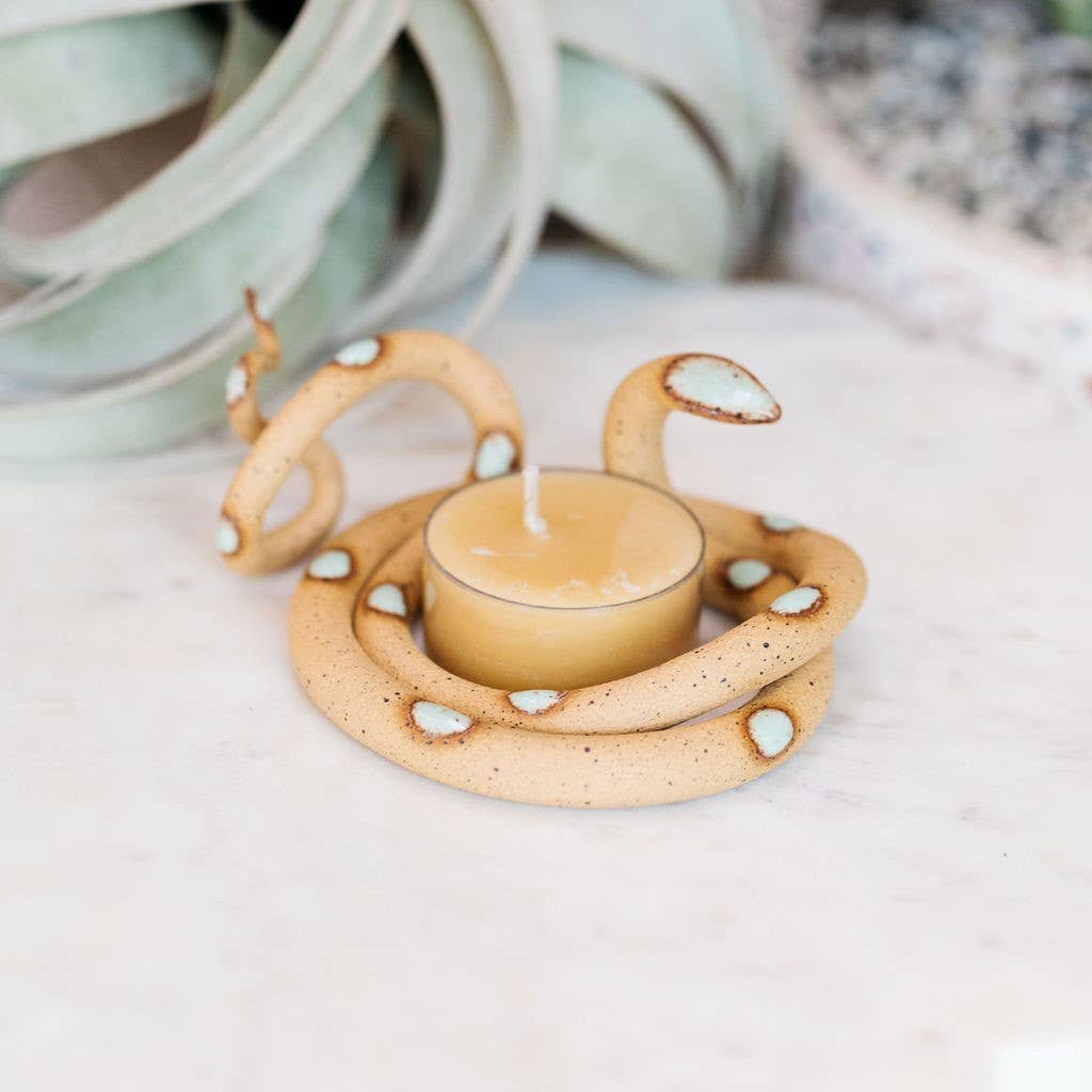 Speckled tan ceramic snake tealight holder with pale aqua spots curled around a beeswax tealight on marble