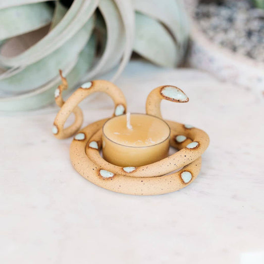 Speckled tan ceramic snake tealight holder with pale aqua spots curled around a beeswax tealight on marble
