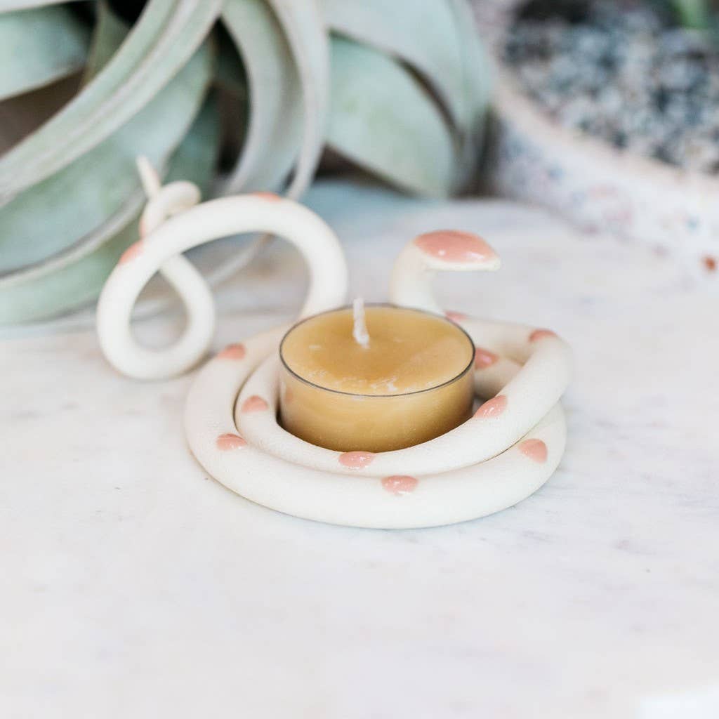 White ceramic snake tealight holder with soft pink spots and a pink head, coiled around a beeswax tealight