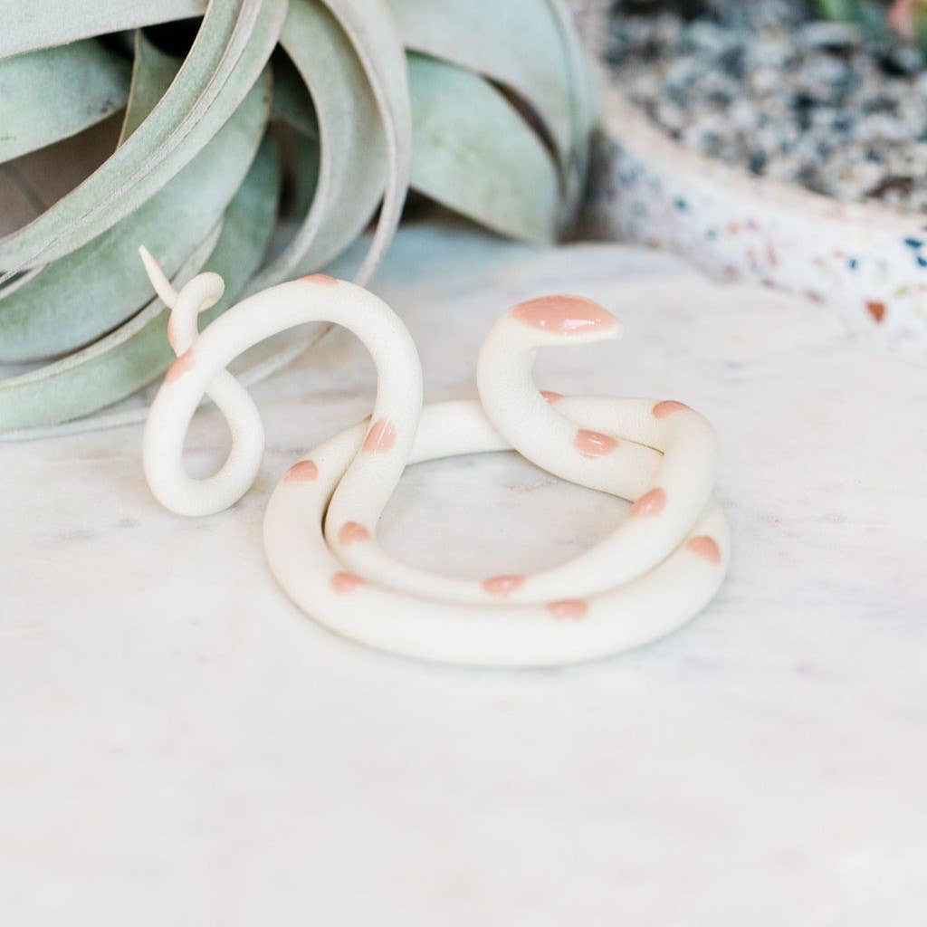 White ceramic snake with peach pink spots, coiled empty with tail curled up, on white marble