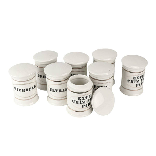 Set of eight white apothecary jars grouped together, one with its lid off, labels like Dipropar and Ultrasicc