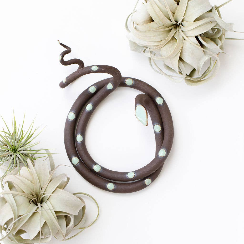 Coiled brown ceramic snake with mint green spots, shown from above among air plants