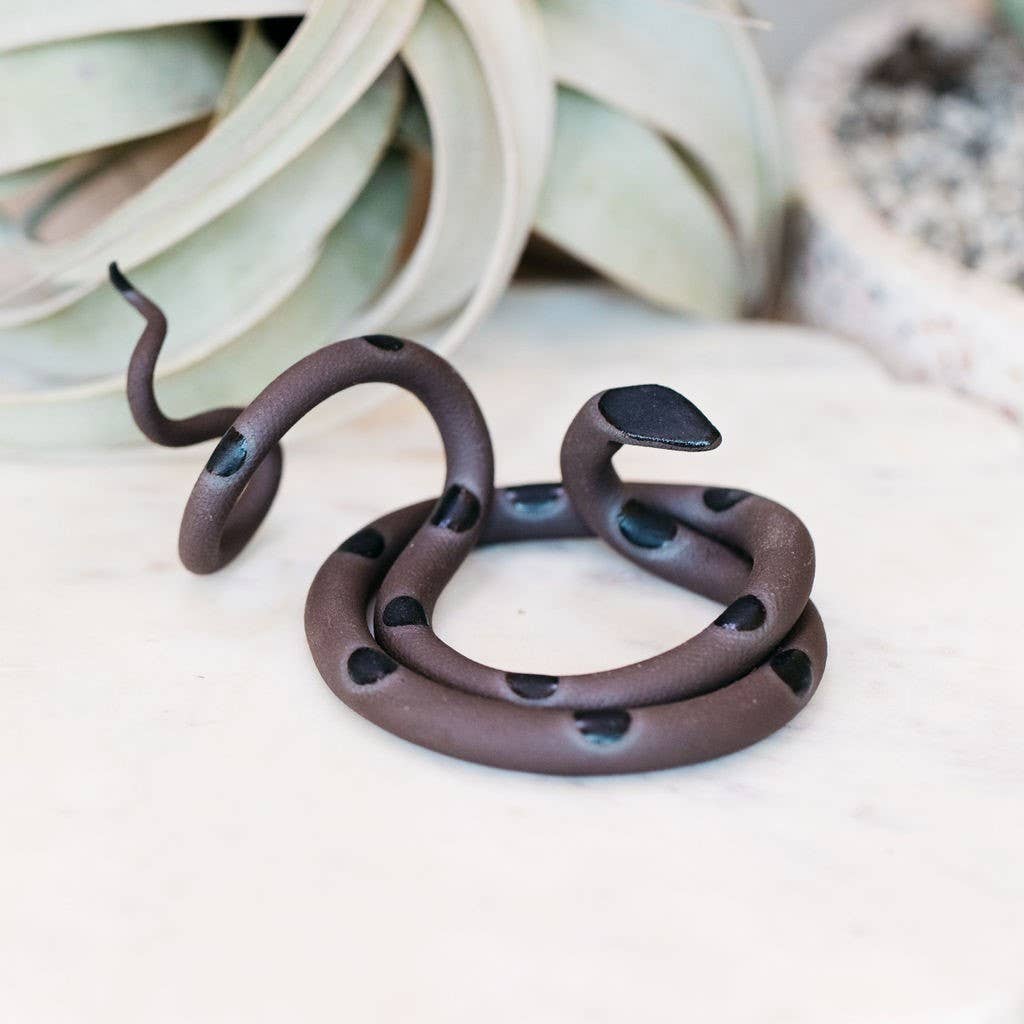 Dark brown ceramic snake with black spots and black head, coiled on a light marble surface