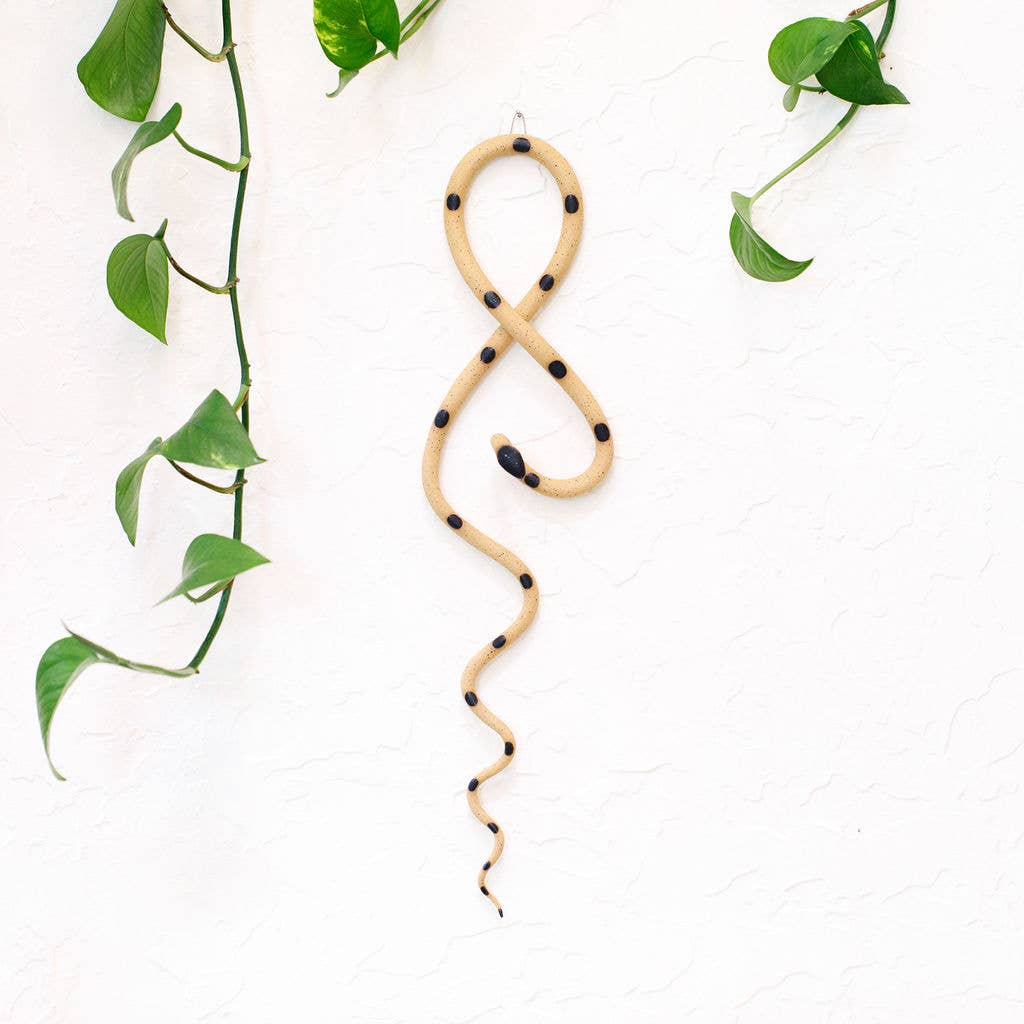 Sandy tan ceramic wall snake with black dots in a looped shape on a white stucco wall