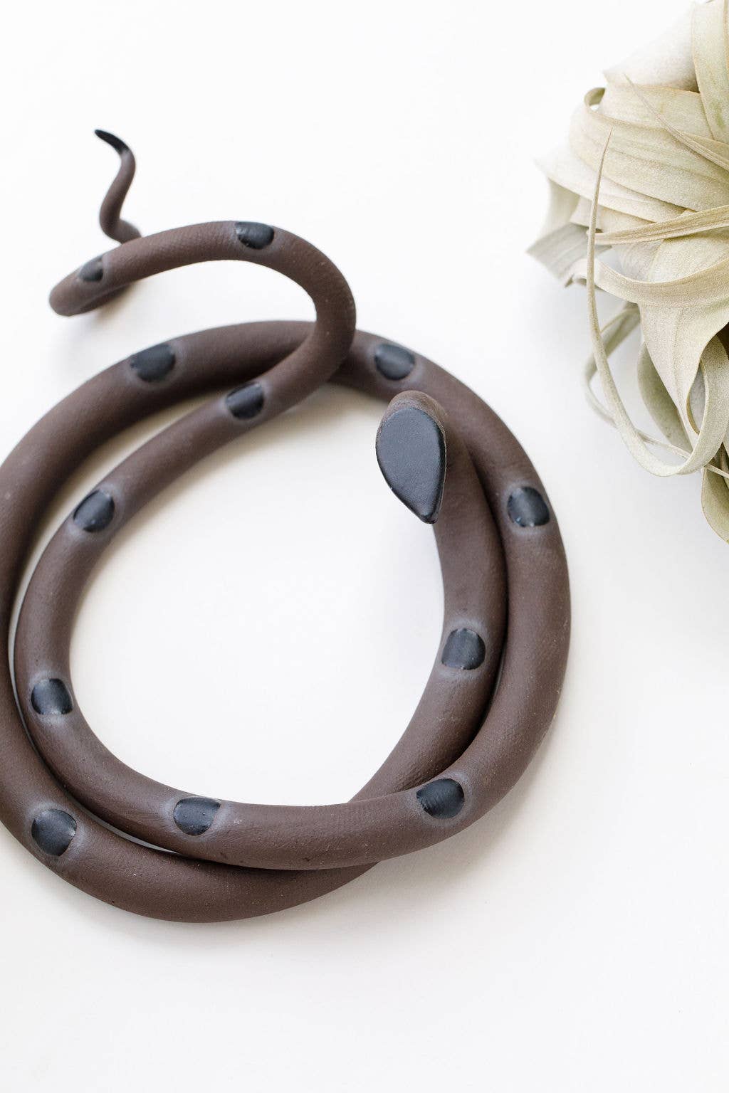 Close-up of a brown ceramic snake with dark gray spots, gray head and curled tail
