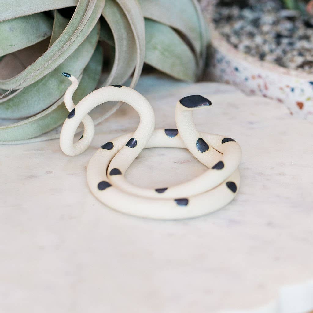 Cream ceramic snake with black spots and black head, coiled empty on a marble surface