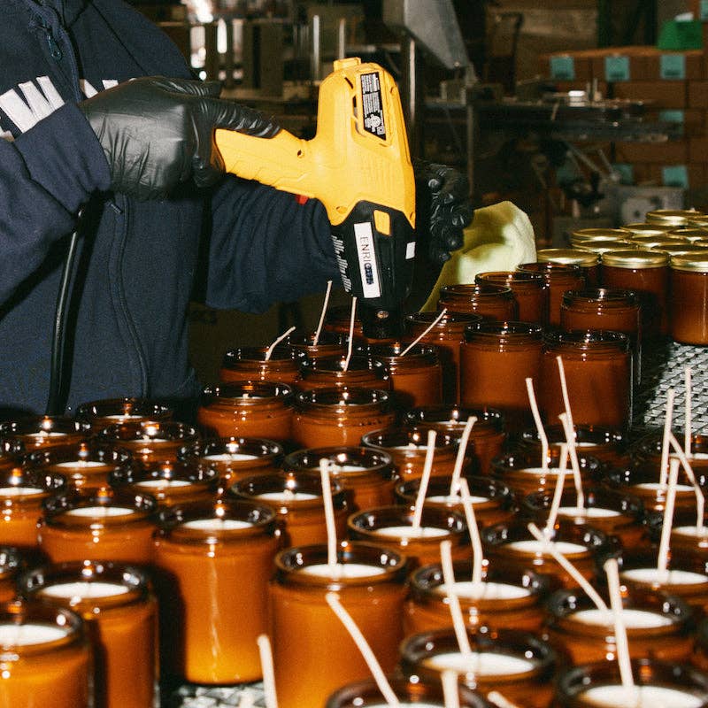 Worker with a glue gun setting wicks in rows of amber candle jars on a production line
