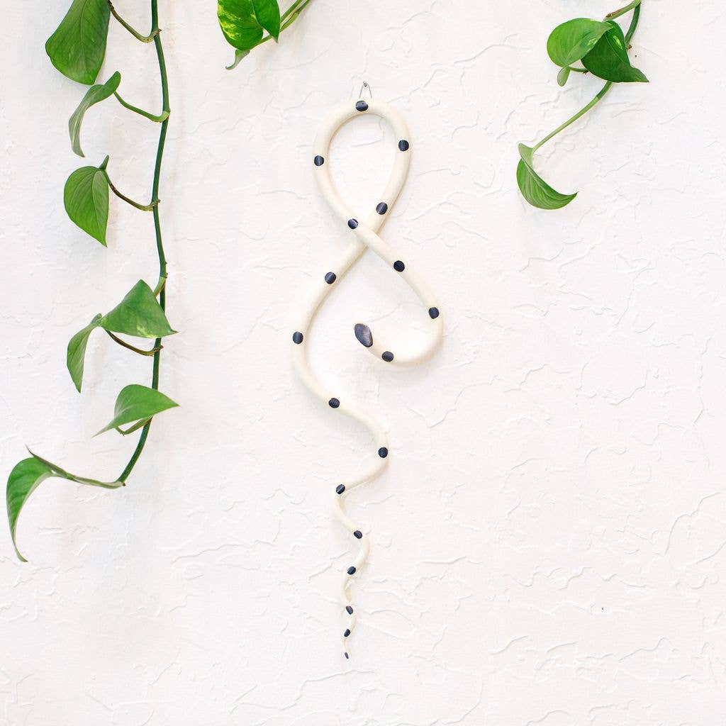 Cream ceramic wall snake with black dots and a dark head, looped and hung on a white wall