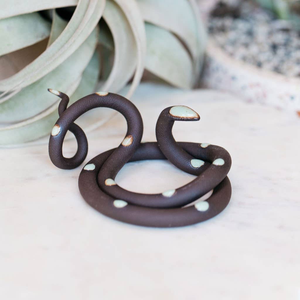 Dark brown ceramic snake with pale mint spots and a mint head, coiled with its head raised on marble