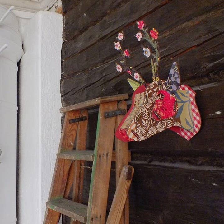Flower Blow-Up deer head mounted on a dark wood wall beside a wooden ladder, side view