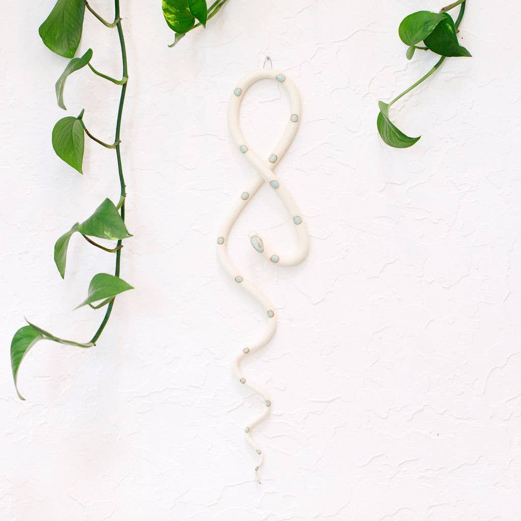 Cream ceramic wall snake with pale mint dots hanging in a figure-eight curl on a white wall