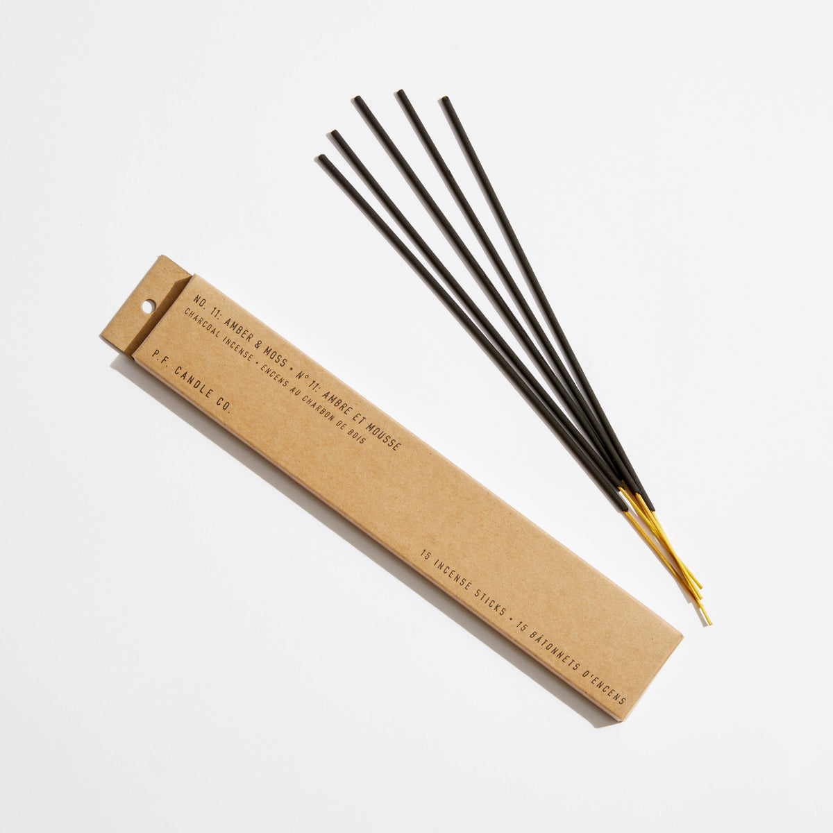 Amber & Moss incense in a kraft paper box beside five black incense sticks with gold-colored tips