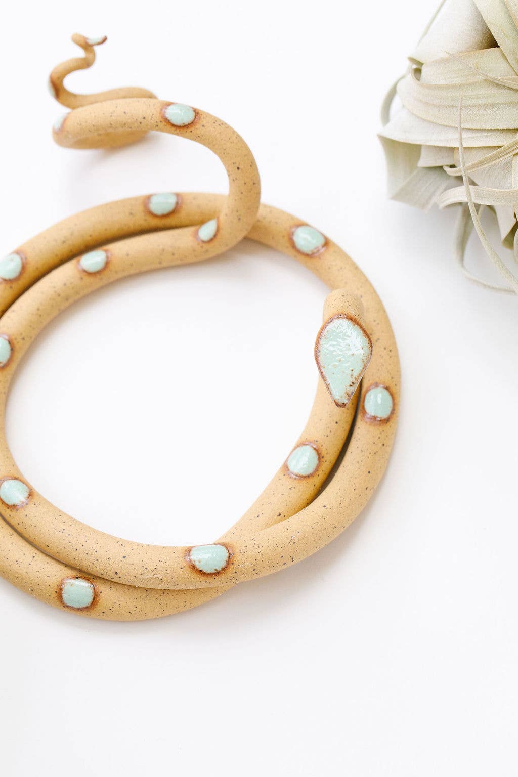 Close-up of a speckled tan ceramic snake with mint green spots and a mint head