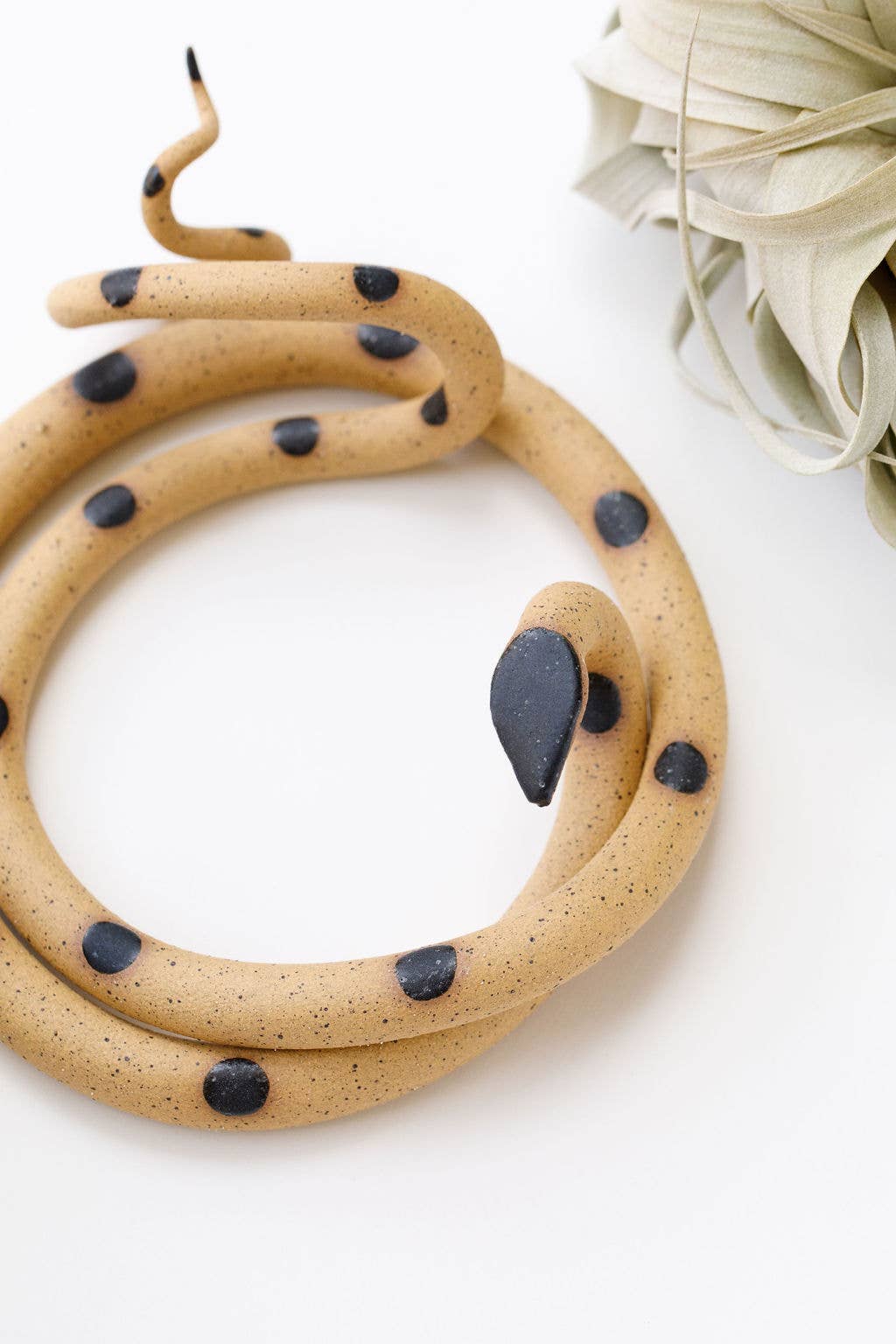 Close-up of a speckled tan ceramic snake with black spots and a raised tail tip
