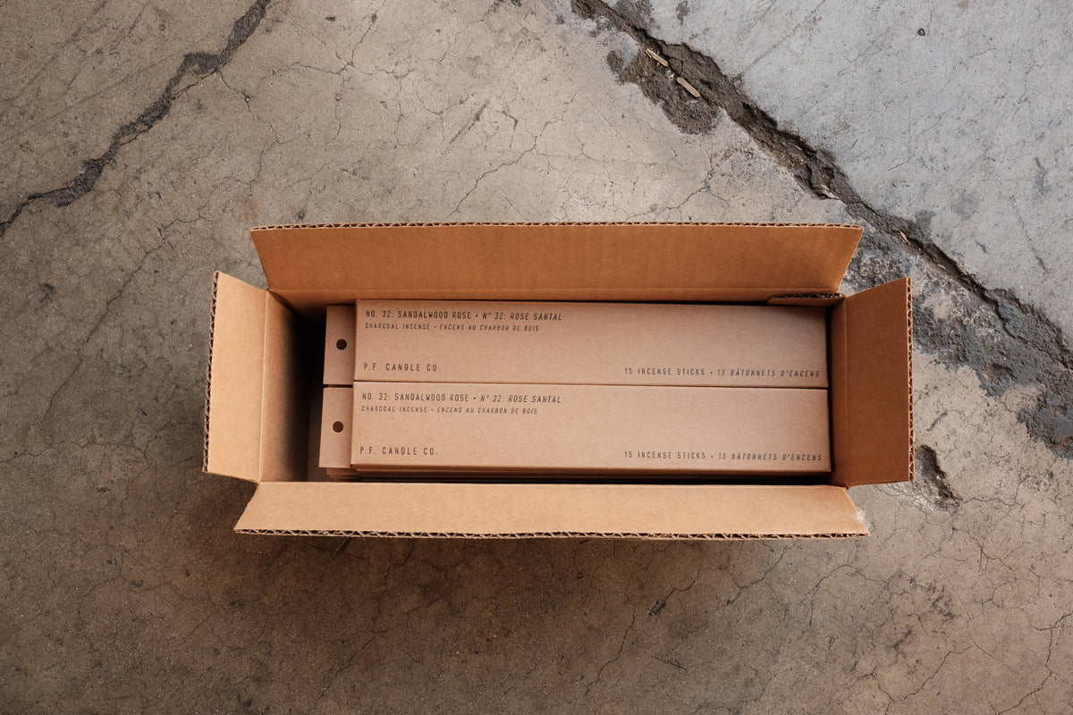 Open shipping carton holding kraft incense boxes, seen from above on a concrete floor