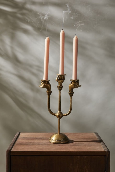 Haunted Hands candelabra holding three peach taper candles with smoke, on a wooden nightstand