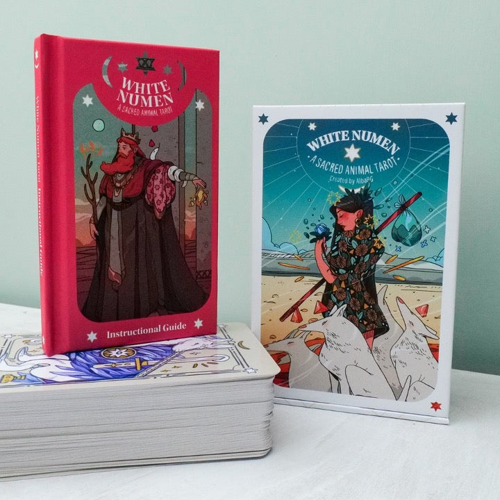 White Numen red instructional guide book standing beside the deck box on a stack of cards
