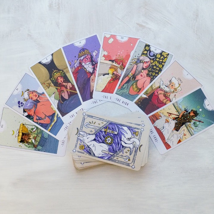 White Numen tarot cards fanned in a semicircle around the deck, top card showing a purple rabbit design