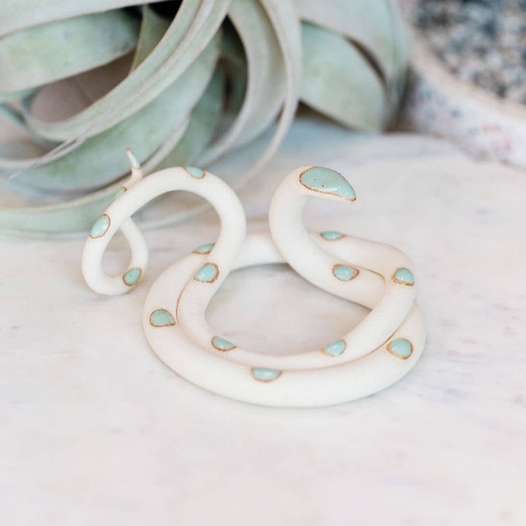 White ceramic snake with mint green spots coiled with raised head on marble beside an air plant