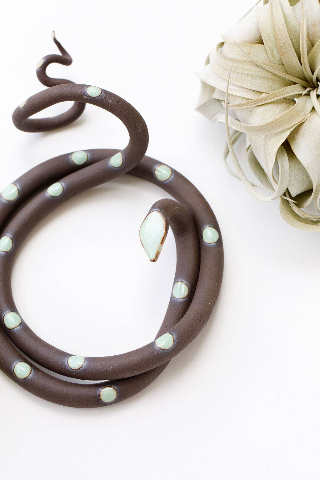 Close-up of a brown ceramic snake with mint green spots and a pale mint head