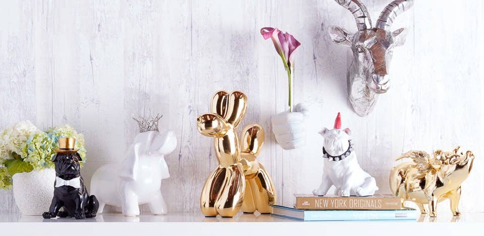 White vase hand holding a pink calla lily on a shelf with gold and white animal figurines
