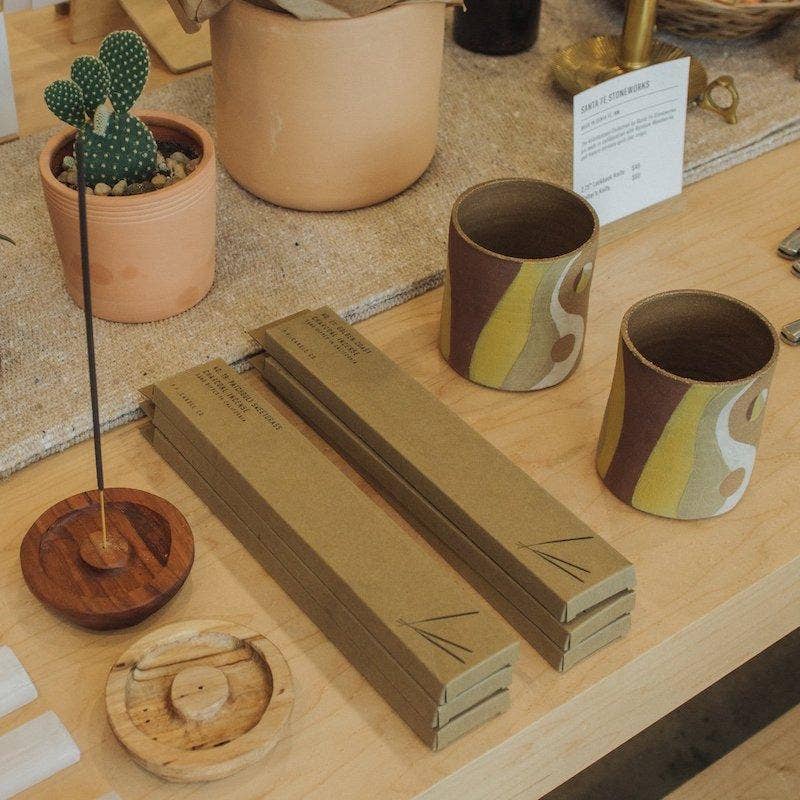 Incense boxes stacked on a shop table with a burning stick in a wood holder and ceramic cups