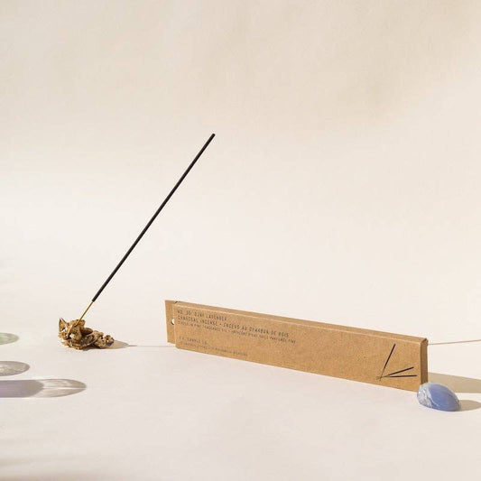 Ojai Lavender incense stick in a brass holder next to its kraft box and a blue stone
