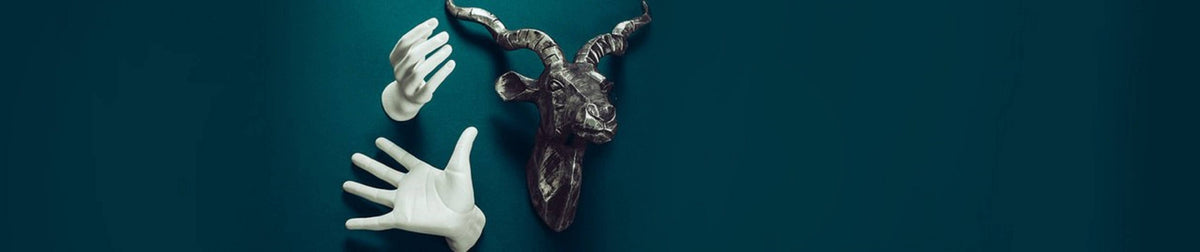 White ceramic hand wall mounts displayed on a dark teal wall beside a dark animal head sculpture