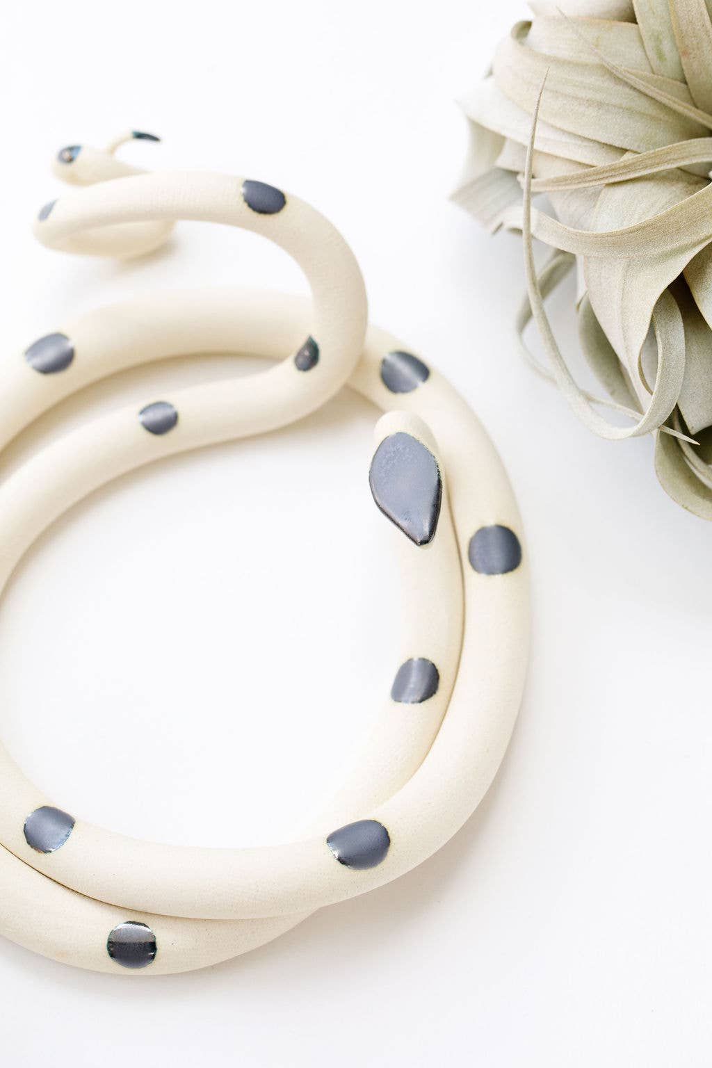 Close-up of a cream ceramic snake with glossy gray spots and a gray head, beside an air plant