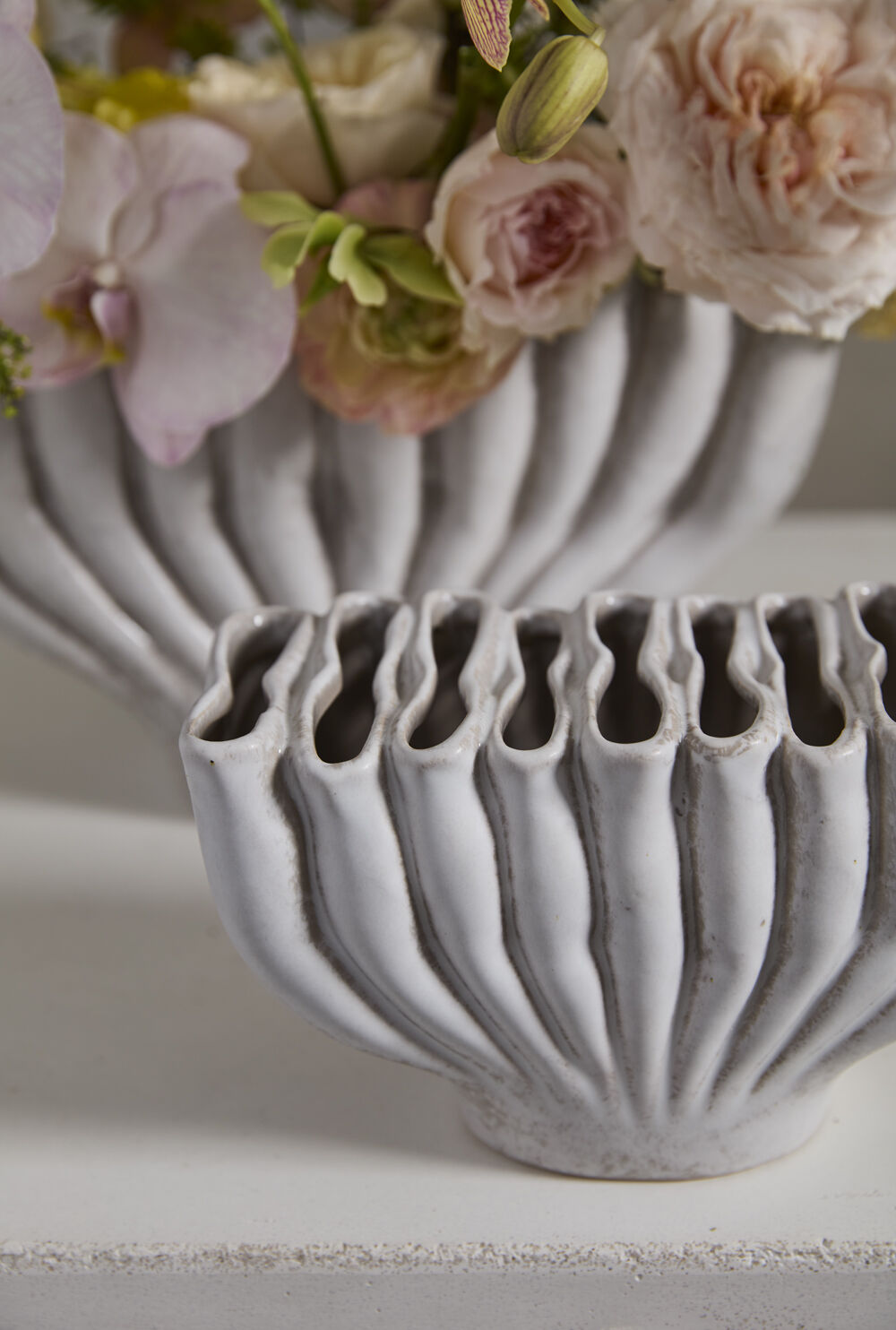 Close-up of the small Clymene vase's wavy slit openings with the larger vase holding flowers behind